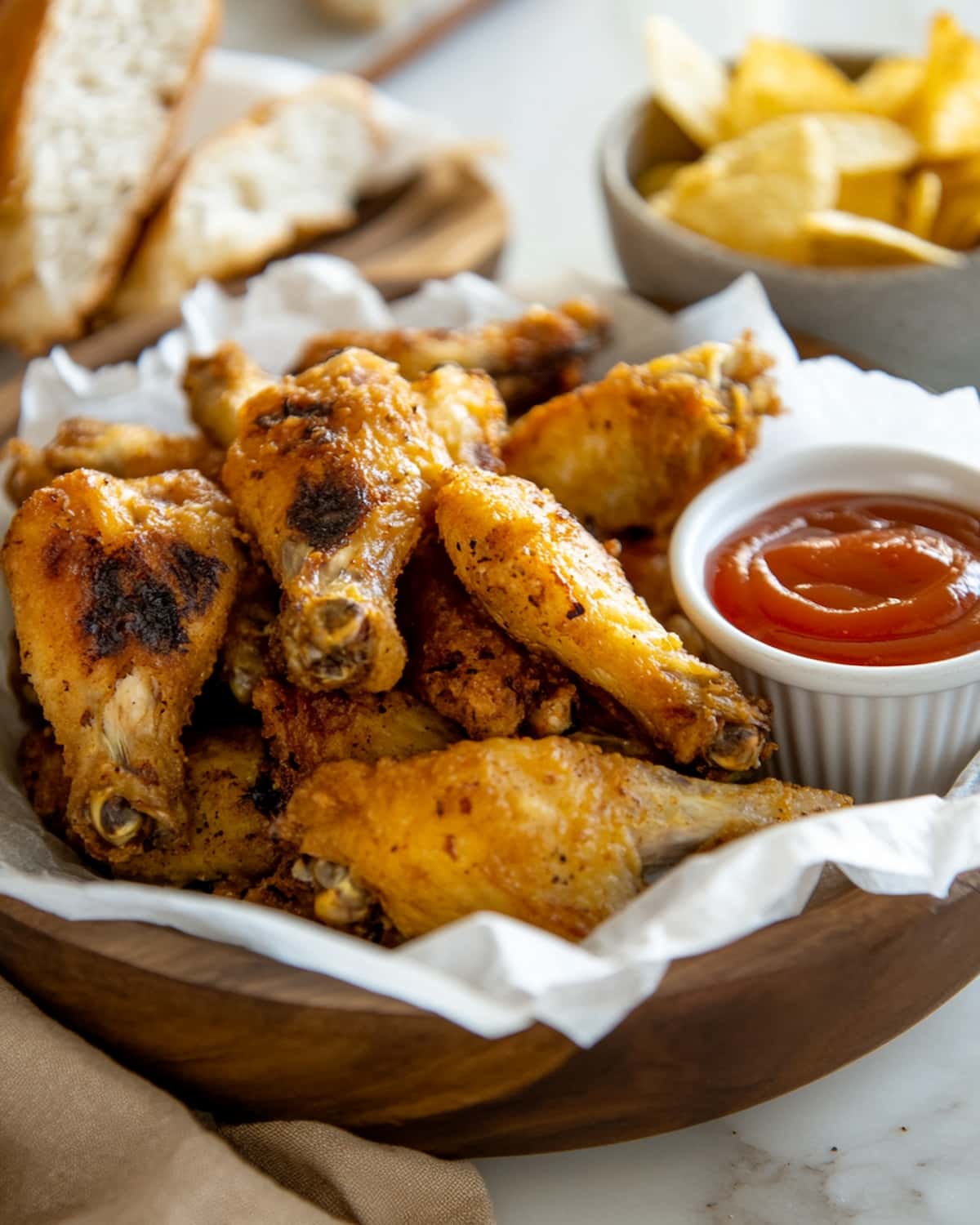 Bol garni d’ailes de poulet au Air Fryer dorées. Servies avec sauce ketchup, pain frais et chips.