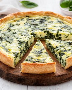 Planche en bois avec quiche aux épinards au Air Fryer, pâte dorée et garniture crémeuse marbrée de vert.