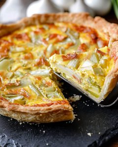 Ardoise avec quiche saumon poireaux au Air Fryer, pâte dorée, garniture crémeuse aux poireaux fondants et morceaux de saumon, part découpée mise en avant