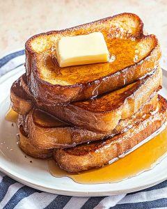 Assiette de French toast au Air Fryer, tranches dorées empilées, nappées de sirop. Un carré de beurre fond sur le dessus, ambiance gourmande.