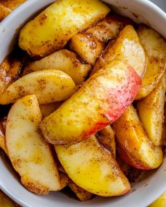 Bol blanc rempli de pommes rôties au Air Fryer, tranches dorées enrobées de cannelle et sucre. Texture fondante et brillante, ambiance réconfortante.