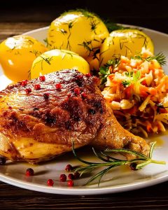 Assiette avec une cuisse de dinde au Air Fryer dorée, servie avec des pommes de terre à l’aneth et une salade de légumes râpés colorée.