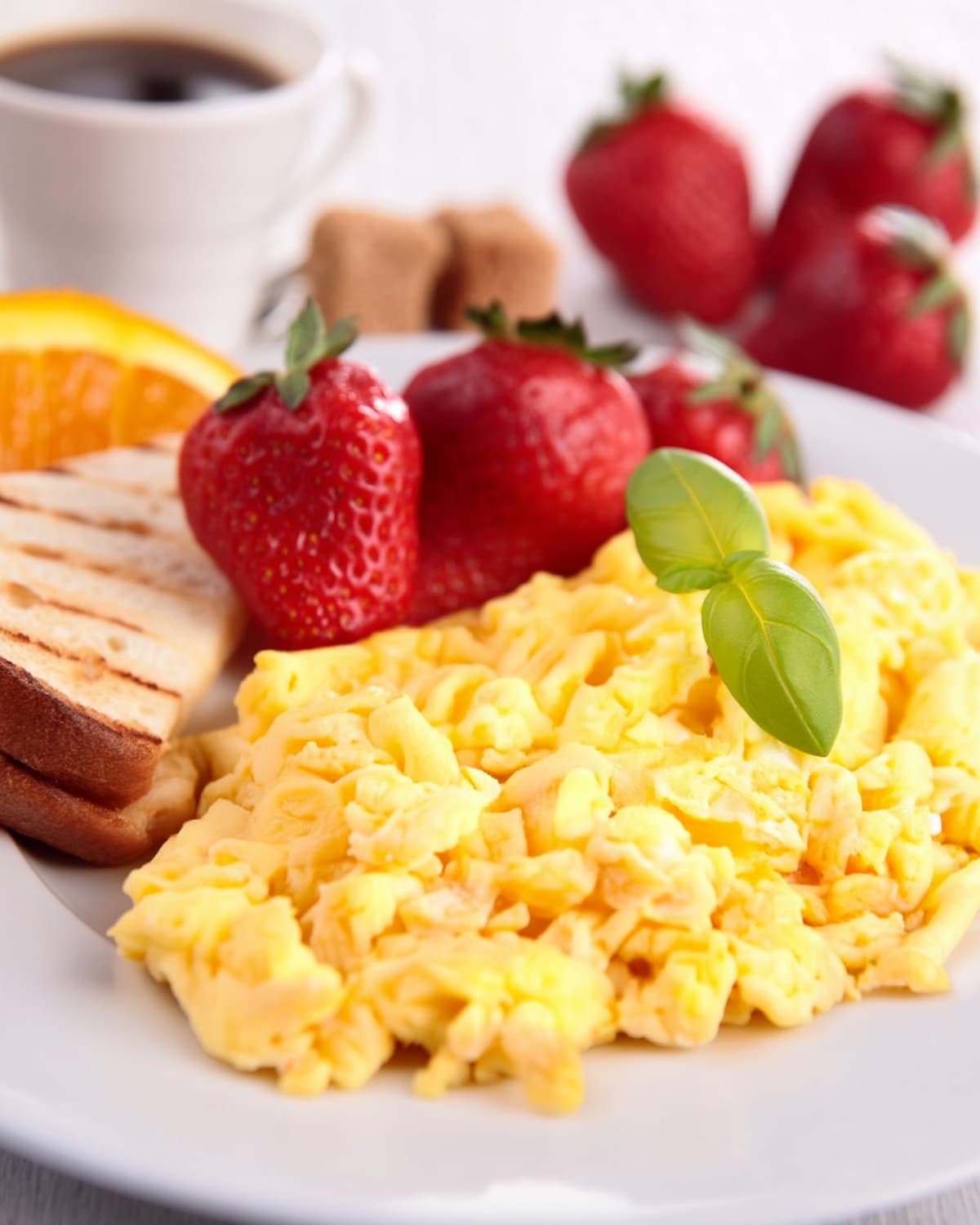 Oeuf brouillé au Air Fryer, accompagné de fraises fraîches, de pain grillé et d'une tranche d’orange.