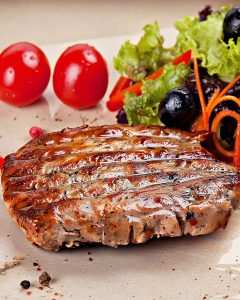 Assiette avec un steak haché surgelé au Air Fryer bien grillé, accompagné de salade fraîche, tomates cerises et olives noires.