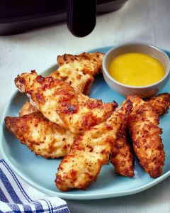 Assiette avec des aiguillettes de poulet au Airfryer, dorées et croustillantes, servies avec une sauce.