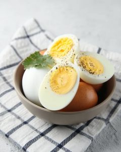 Bol contenant des œufs durs au Airfryer, dont un coupé en deux révélant un jaune bien cuit, assaisonné de poivre et décoré d’une feuille de persil.