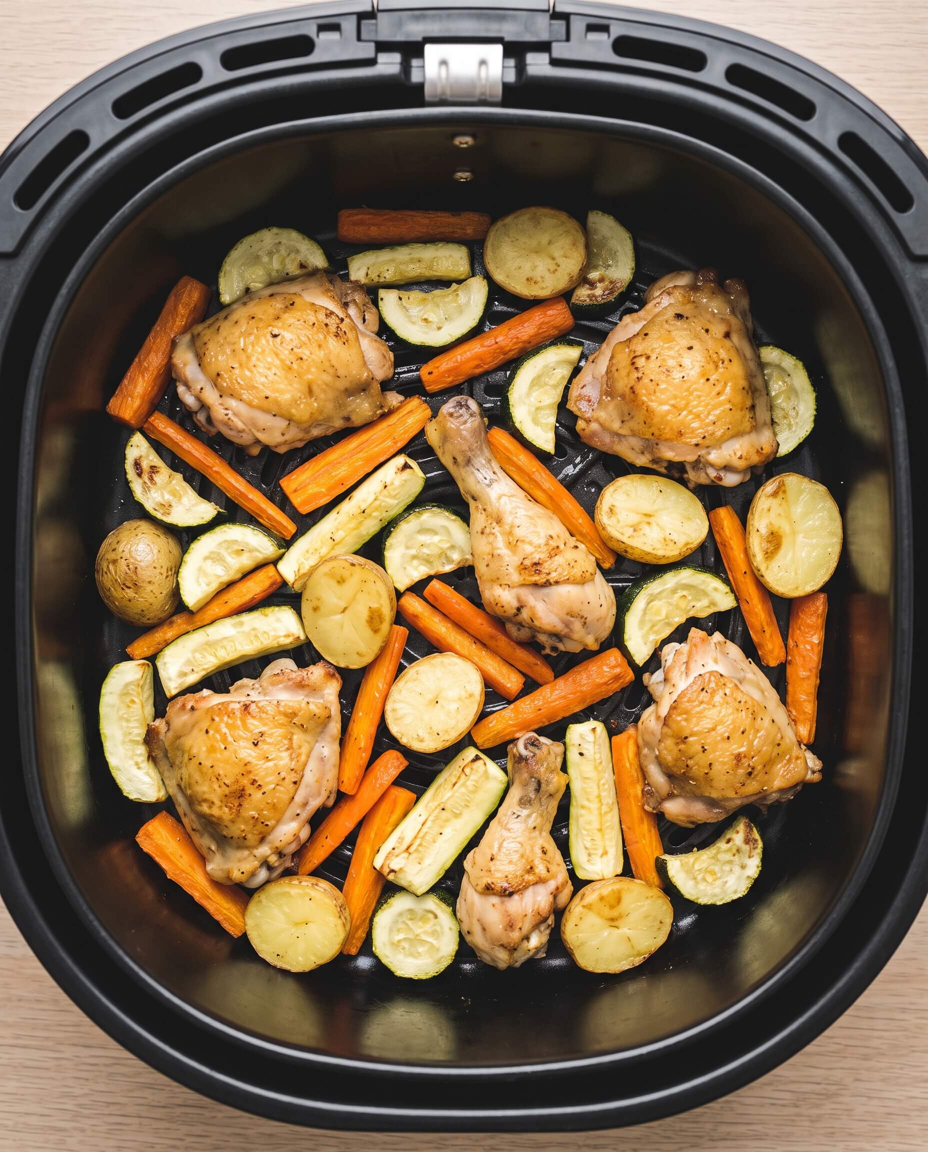 Panier d’air fryer vu de dessus, garni sur une seule couche de poulet doré, carottes, courgettes et pommes de terre