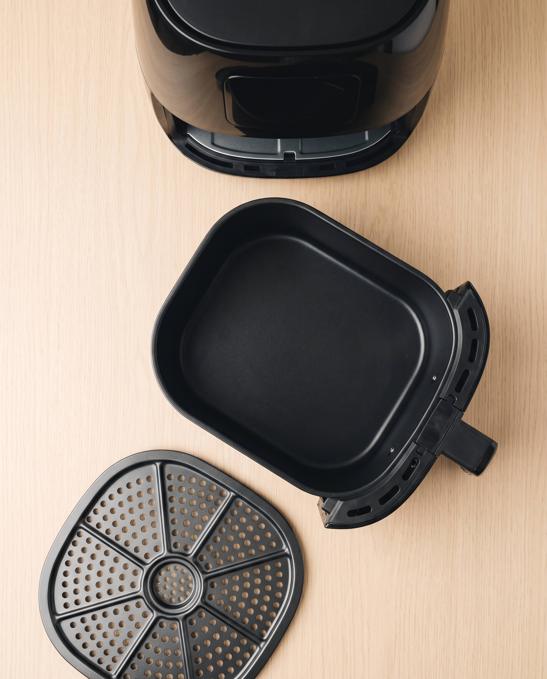 Cuve, panier et grille perforée d'un air fryer posés séparément avant le premier lavage