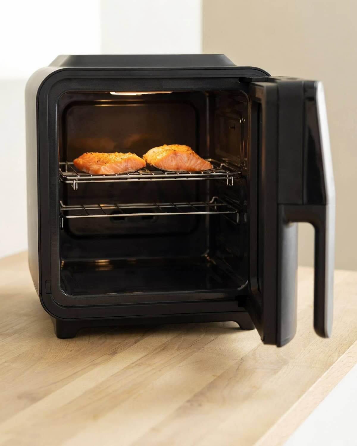 Air fryer four porte ouverte, deux pavés de saumon sur une grille en inox à mi-hauteur de la cavité