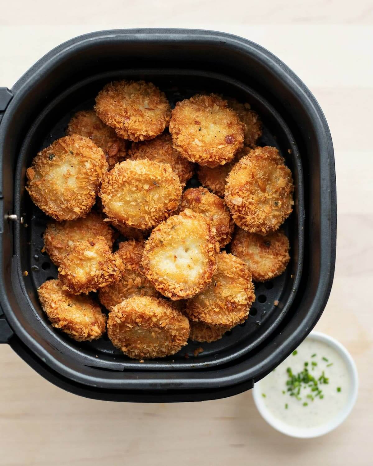 Nuggets de poulet dorés et croustillants dans le panier d'un air fryer, avec une sauce à la ciboulette