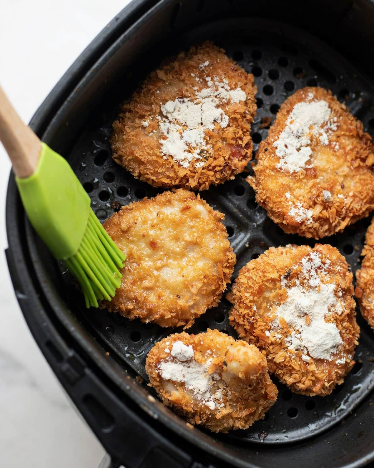 Gros plan sur des morceaux de poulet panés sortis de l’air fryer, avec des plaques de farine blanche et poudreuse faute d’huile