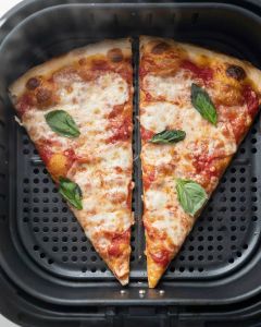 Deux parts de pizza réchauffées à plat dans le panier d'un air fryer, fromage refondu et basilic frais