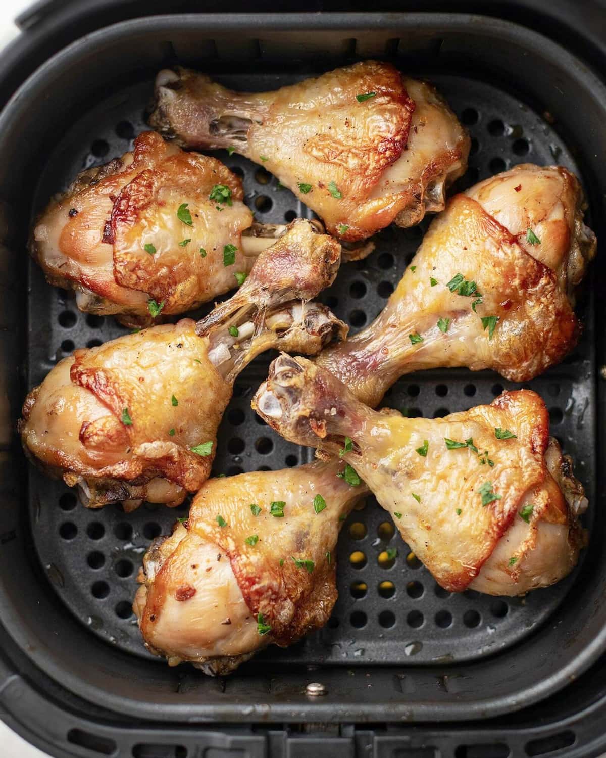 Pilons de poulet dorés posés sur la grille perforée d'un panier d'air fryer, parsemés de persil