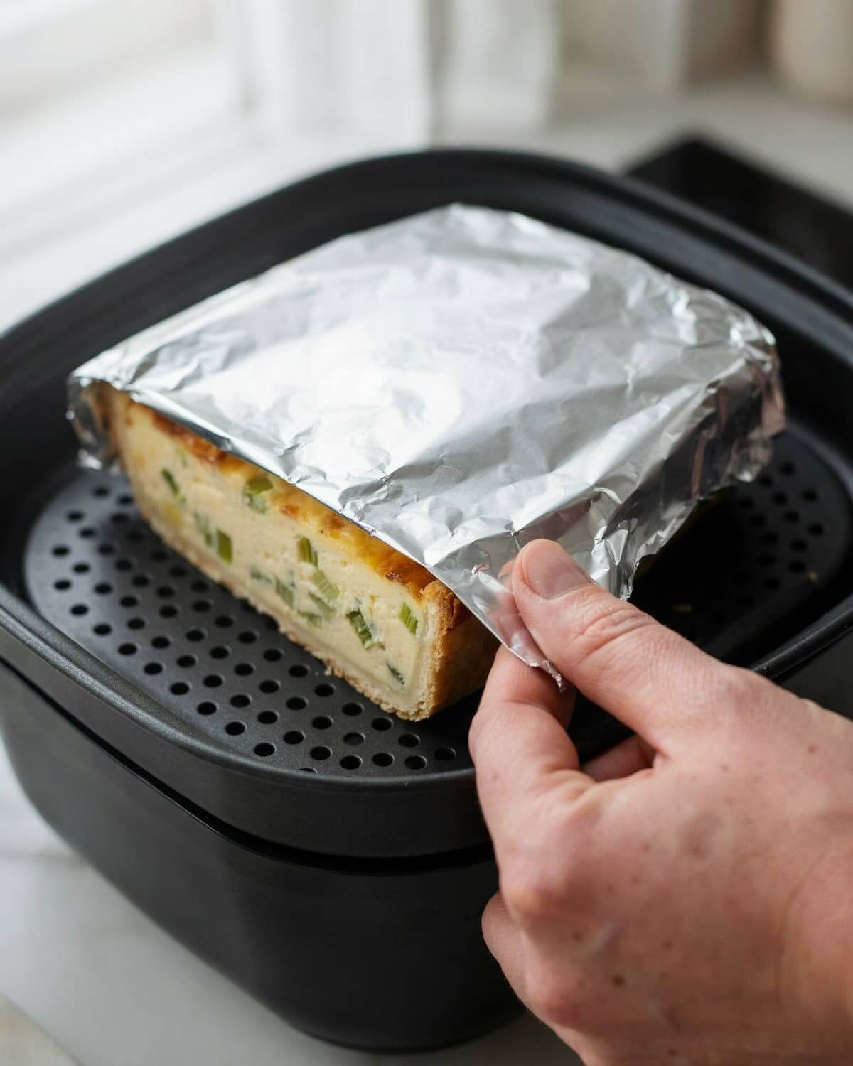 Part de quiche dans le panier d'un air fryer, coiffée d'aluminium bien pincé autour des bords